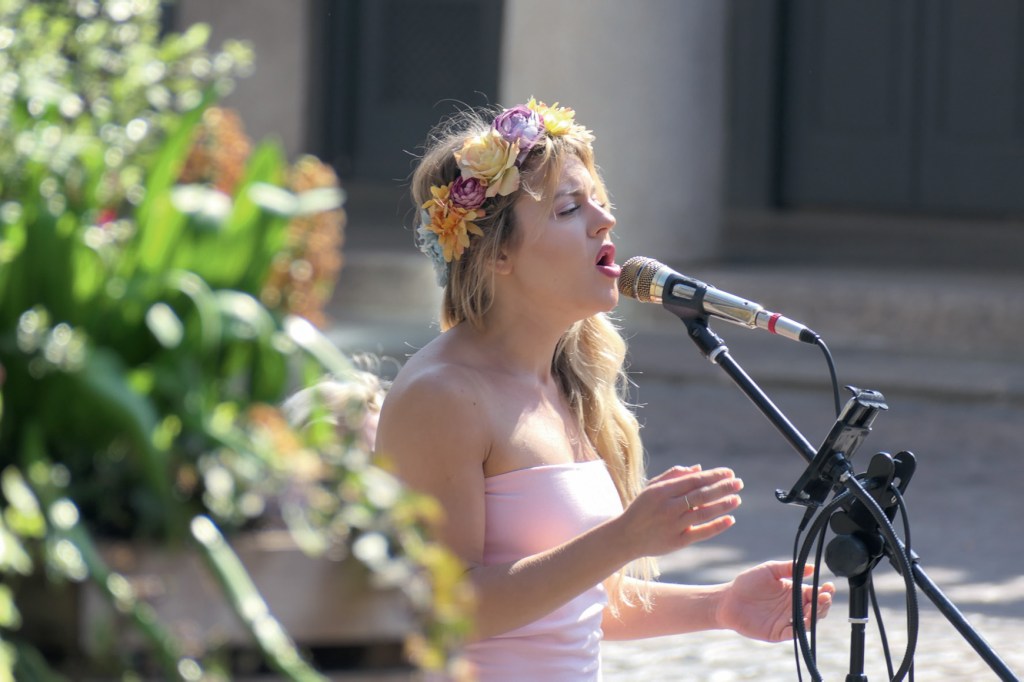 Panasonic Lumic FZ 1000 II Sample image. Woman dressed in pink and wearing a flower wreath singing in a microphone outdoor.