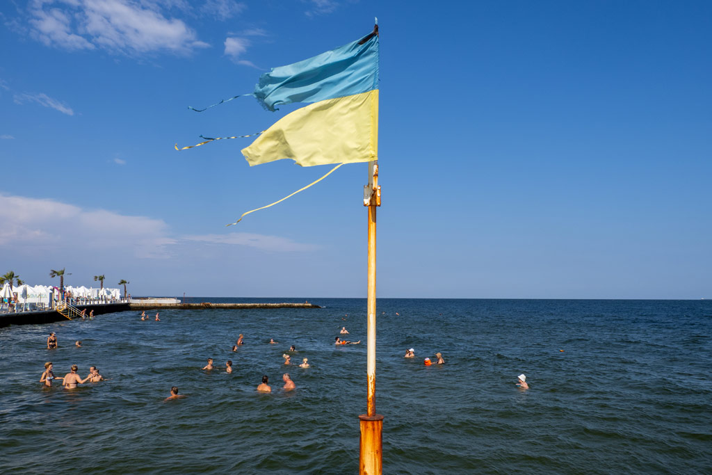 A ragged Ukrainian flag flies beside bathers in the Black Sea, Odessa. Photo: Peter Dench