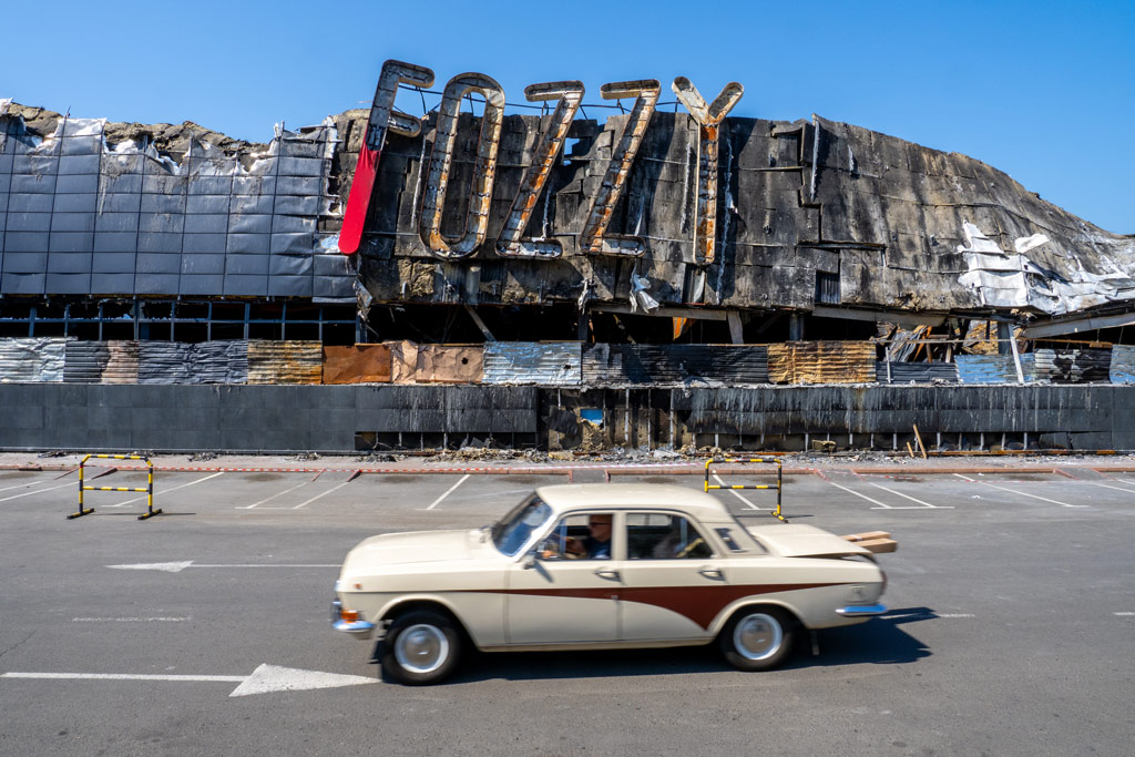 A Fozzy group supermarket destroyed after a missile attack, an old car passing in front