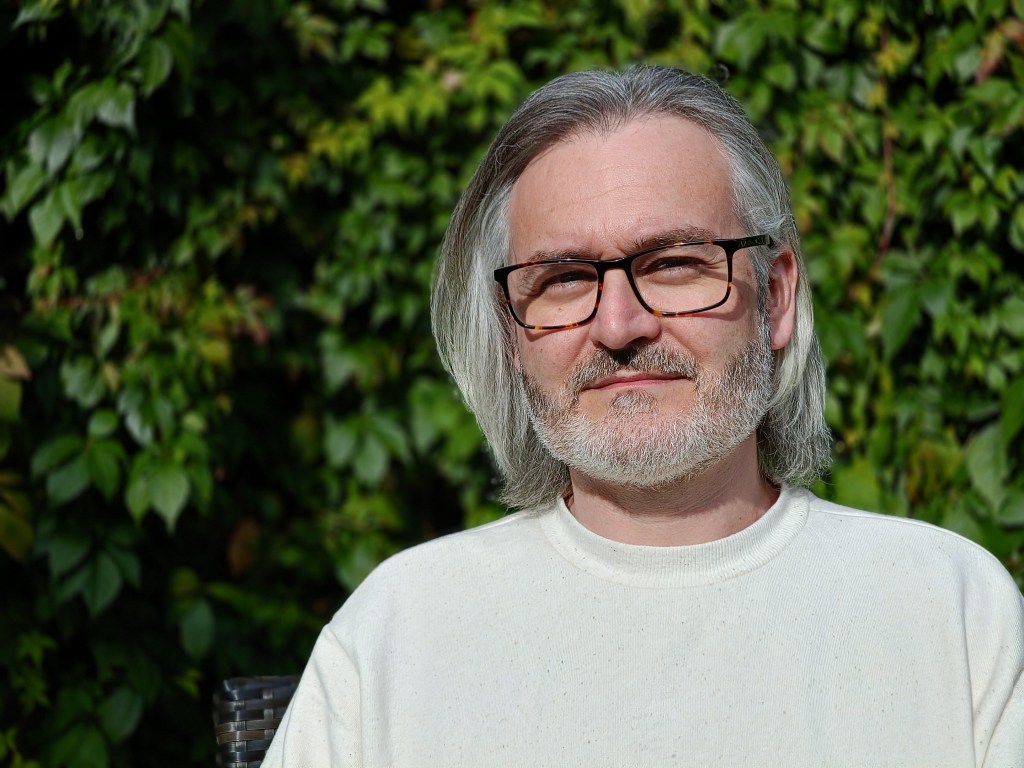 Oppo Reno 10 portrait mode sample image, Portrait of a man with white shoulder length hair black glasses and short beard. credit: Amy Davies