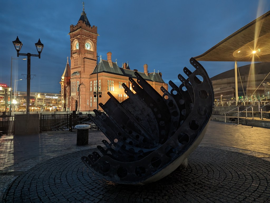 Google Pixel 7 Pro Night Sight sample image, modern sculpture at night in the background an illuminated clocktower