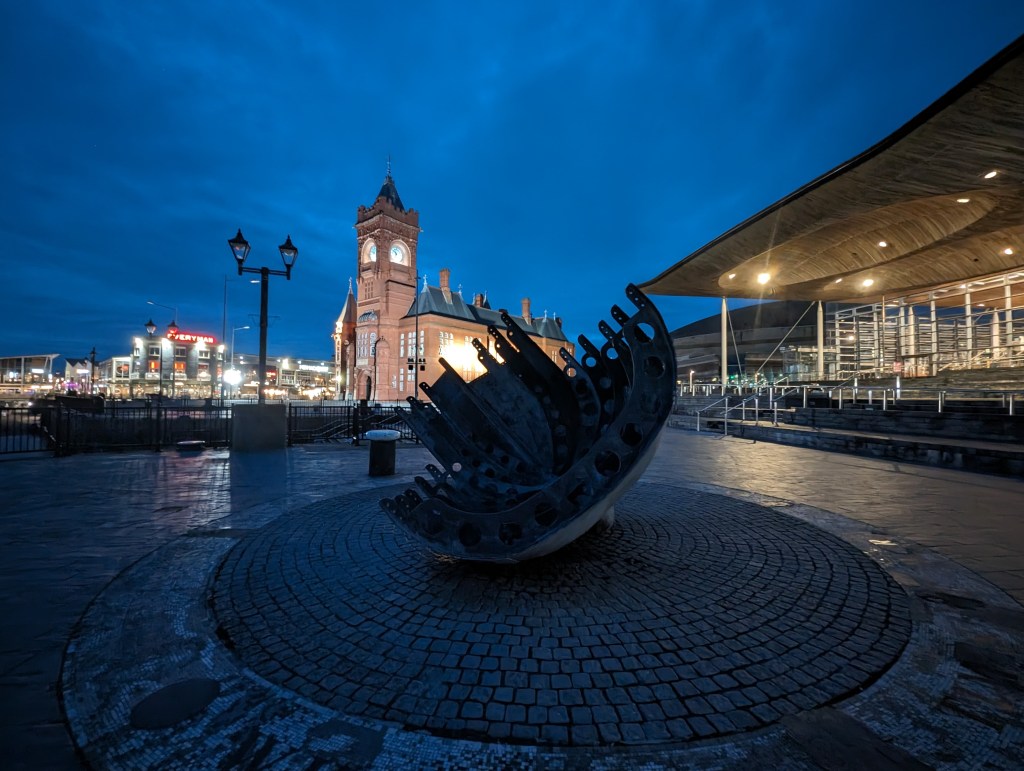 Google Pixel 7 Pro Night Sight Ultrawide lens sample image, modern sculpture at night in the background an illuminated clocktower