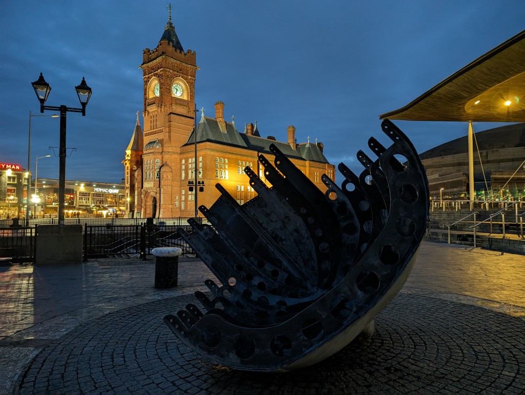 Google Pixel 8 Pro Night Sight sample image, modern sculpture at night in the background an illuminated clocktower