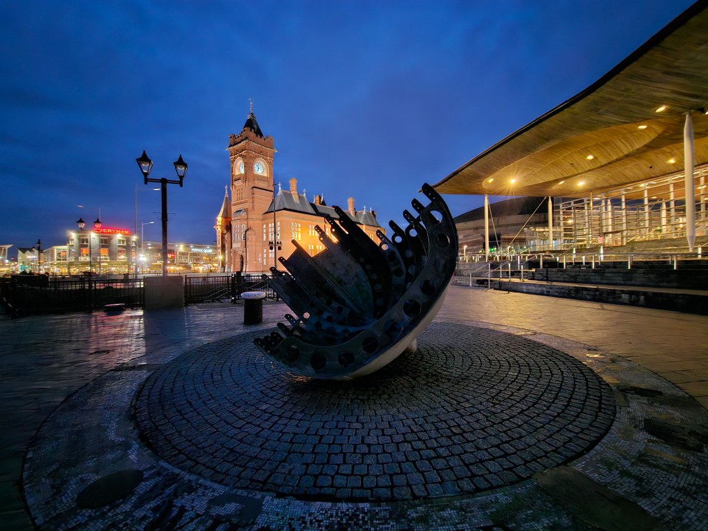 Samsung S23 Ultra ultrawide lens, night mode sample image, modern sculpture at night in the background an illuminated clocktower 