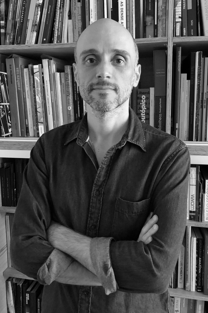 Black and white portrait of Thyago Nogueira in front of a bookshelf