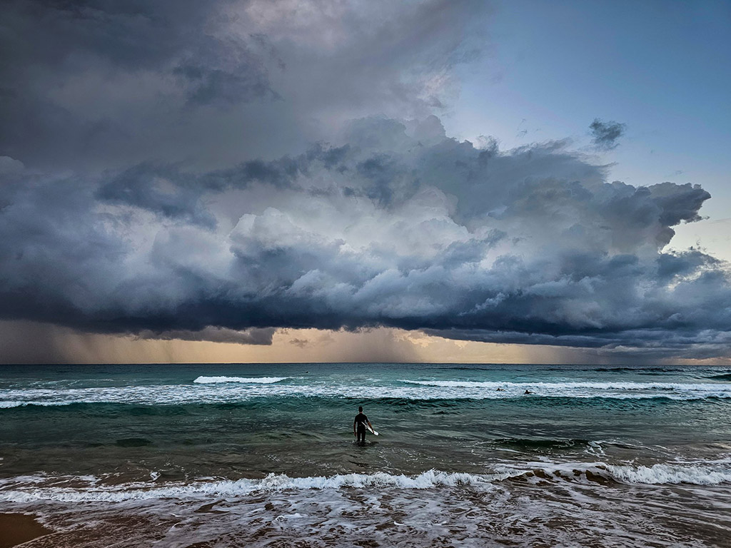 a surfer in Sydney, Australia, contemplating the heavy convective clouds that announce an impending storm.