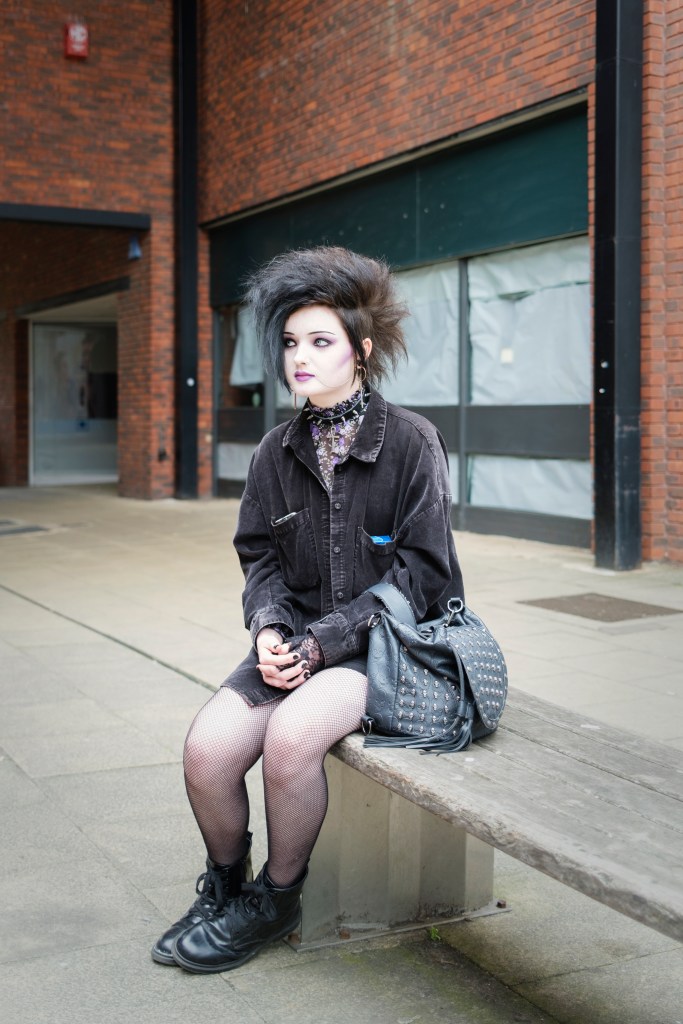 portrait of a young punk girl sitting on a street bench