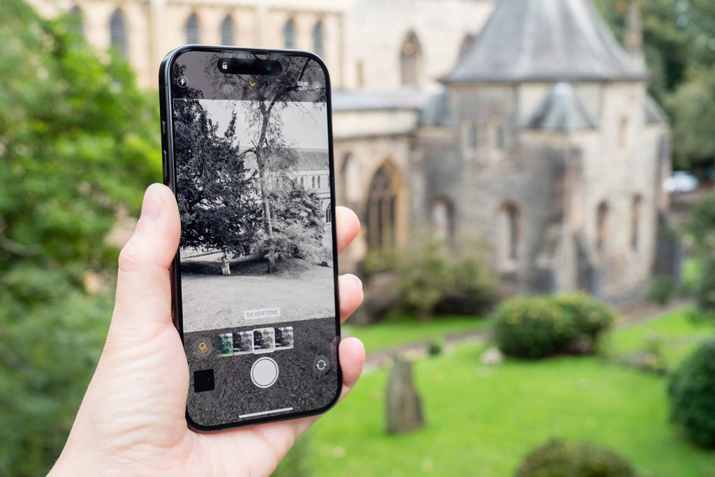 iPhone photography tips. The view of a cathedral in the background is displayed on an iPhone in hand, live view shows how a black and white filter changes the image. 
