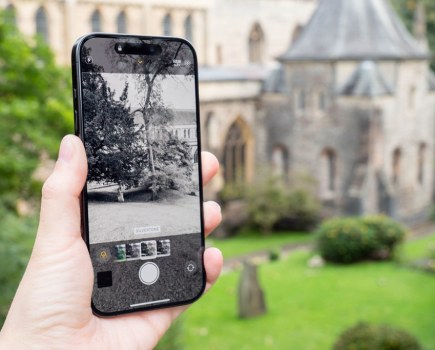 The view of a cathedral in the background is displayed on an iPhone in hand, live view shows how a black and white filter changes the image.