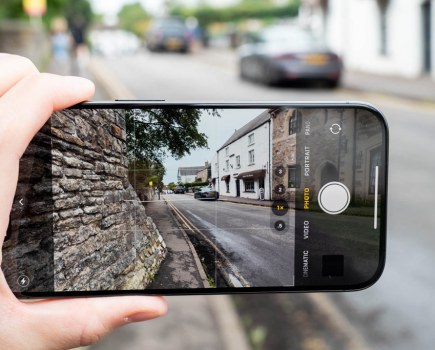 iPhone held up in hand displaying street view with adjacent stone wall.