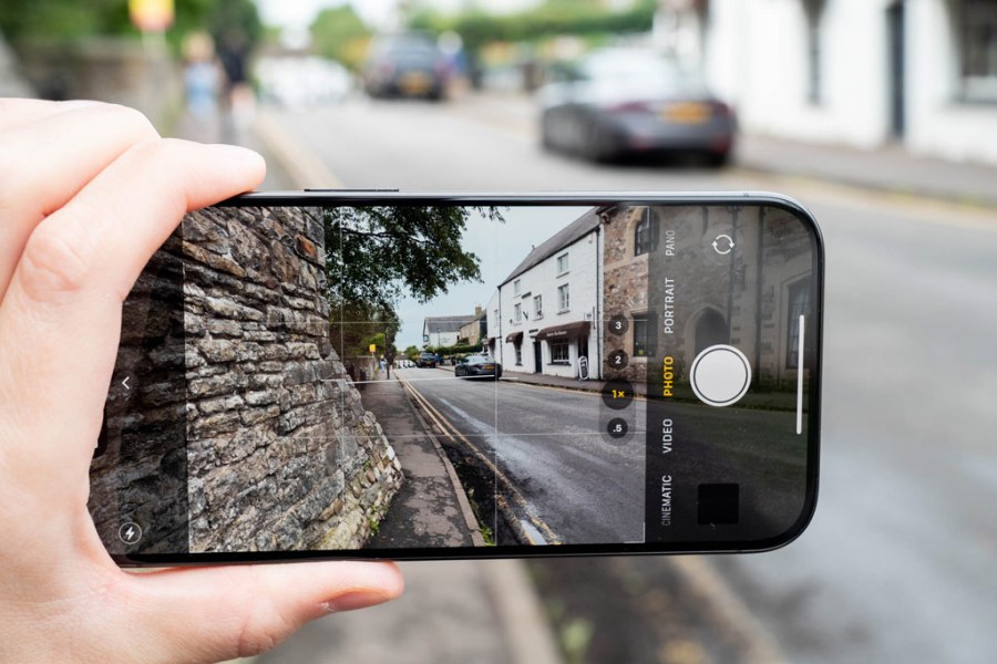 iPhone held up in hand displaying street view with adjacent stone wall.