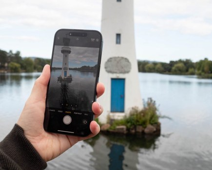 iPhone 15 Pro, in hand displaying an image of a lighthouse