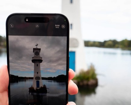 iPhone 15 Pro, in hand displaying an image of a lighthouse, in the background the same scene showing
