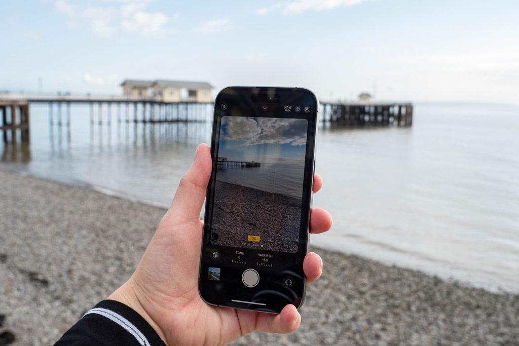 iPhone photography tips. Iphone in hand cool picture style selected, displaying the view in the background of the sea with a pier 