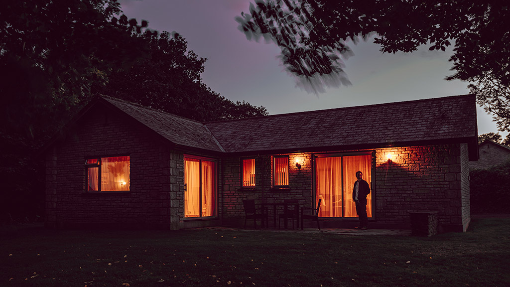 deceptively simple but imaginative image of bungalow in low night light lit up inside