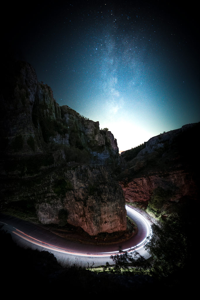 Milky way and a narrow canyon, in the bottom, lighttrails from cars passing