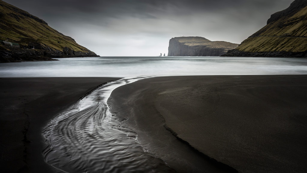 dark seascape with a small stream leading into the water, on the sides cliffs frame a small bay, International Landscape Photographer of the Year 2023 competition