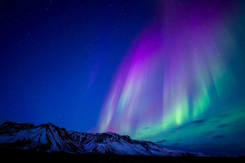 Leica M11 sample image: Purple and green Northern lights above snow capped mountains