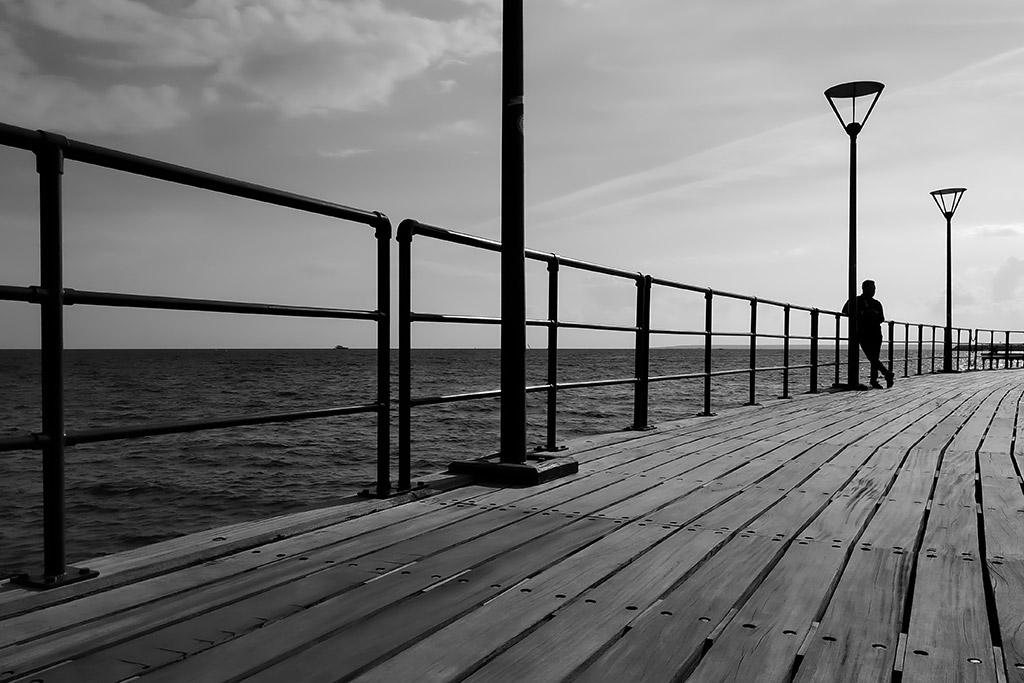 the urbanite has travelled to the seaside, standing alone on a pier. black and white silhouette smartphone picture of the week
