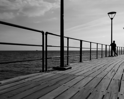 the urbanite has travelled to the seaside, standing alone on a pier. black and white silhouette smartphone picture of the week