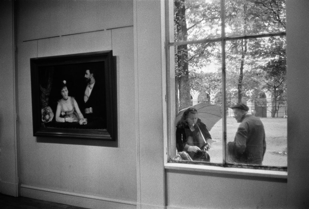 Joel Mayerowitz, a gallery interior with a painting of a couple on the wall, through the window of the gallery we see a real life couple