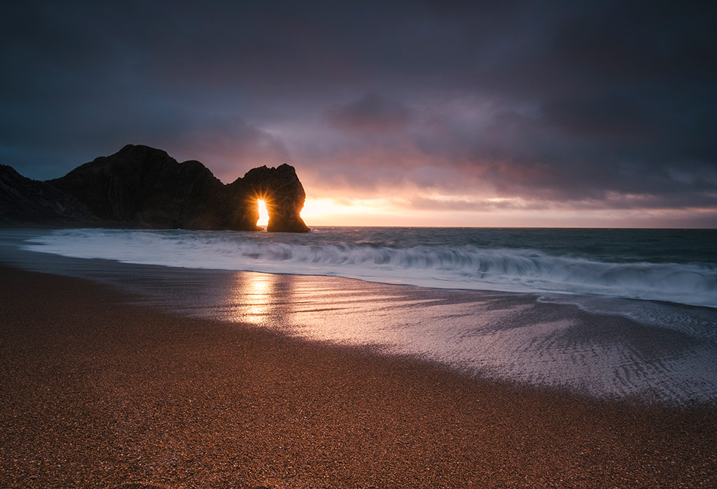 Durdle Door, Dorset. Just as day breaks 
across the coast, a small gap on the horizon allows the light to flood through the arch 
Fujifilm X-T3, 14mm, 0.5sec at f/18, ISO 200