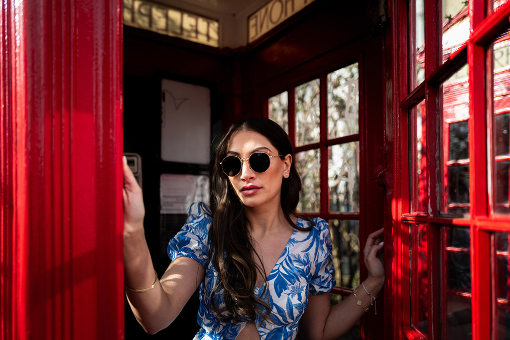 woman in blue floral dress standing in the door of red telephone box