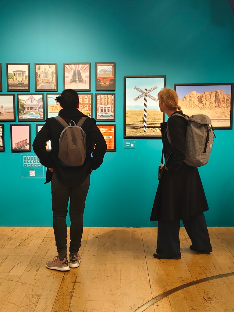 Photo taken indoors of people looking at photos in the Accidentally Wes Anderson exhibition in London