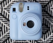A blue Fujifilm Instax Mini 12 against a black and white patterned background