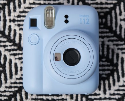 A blue Fujifilm Instax Mini 12 against a black and white patterned background