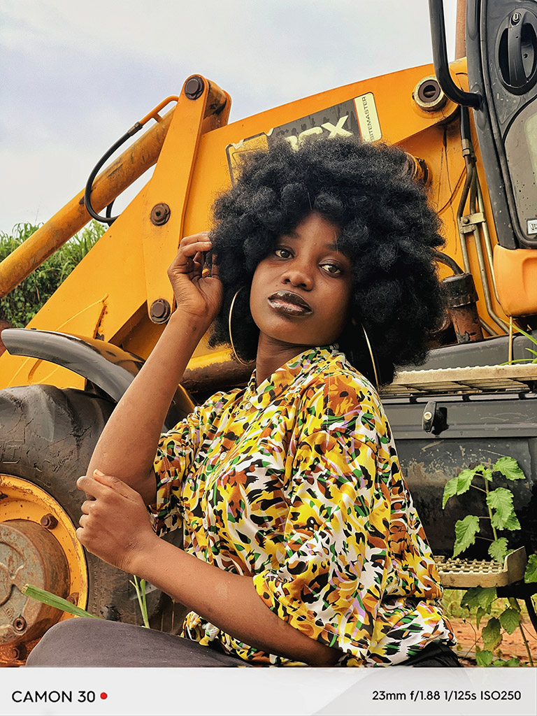 portrait of a dark skinned woman in yellow floral top next to yellow tractor equipment