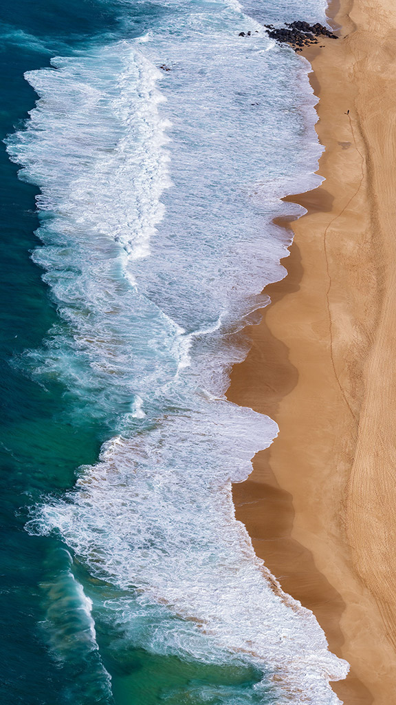 birds eye view aerial photography of waves on  the beach, one single person at the top of the image in view