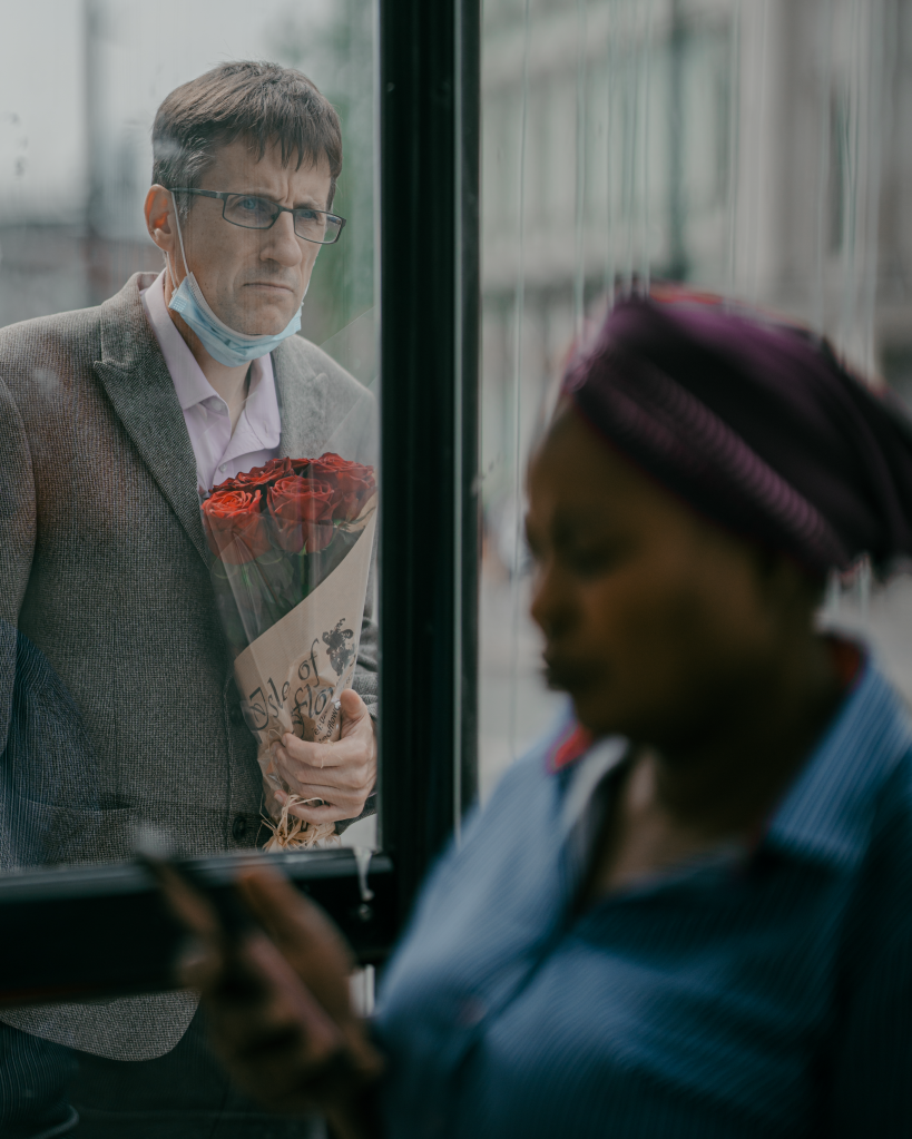 street image looking out of a window man with mask on commute, woman on her phone in foreground hasselblad masters winners