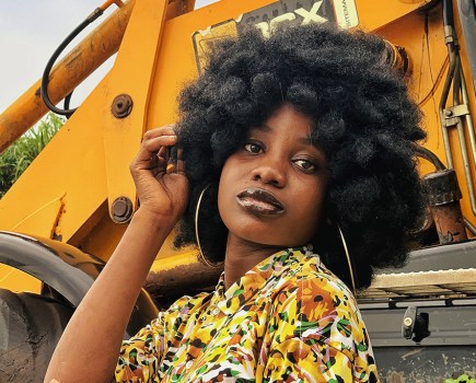 portrait of a dark skinned woman in yellow floral top next to yellow tractor equipment taken on tecno smartphone