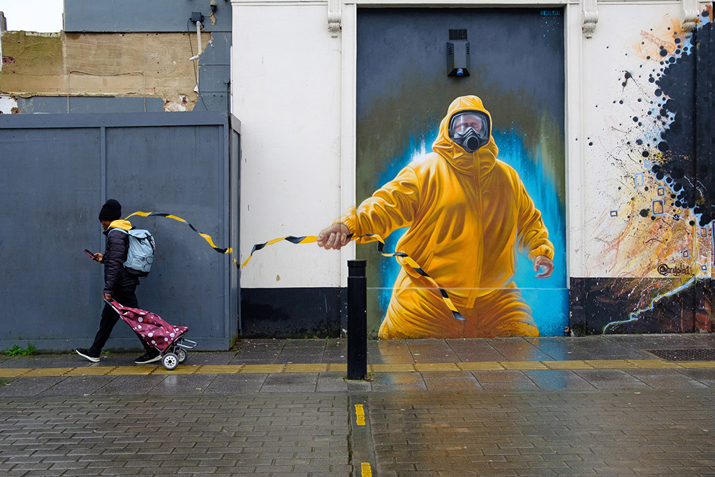 winner of the apoy urban life 2024 round image of person walking past street art with  black and yellow tape 