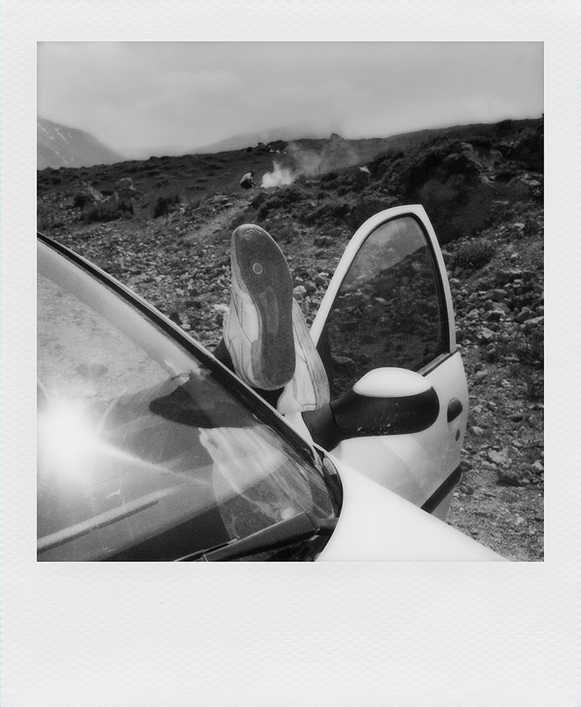 polaroid of car with door open and persons feet leaning on door