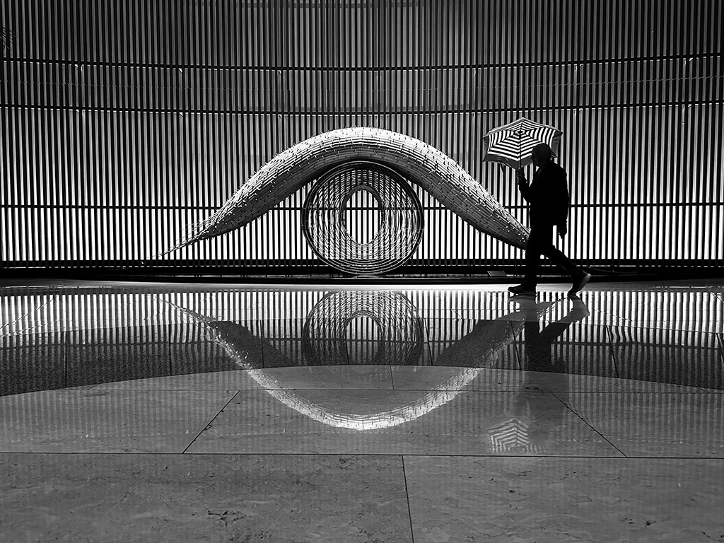 person with striped umbrella walking past striped texture building 