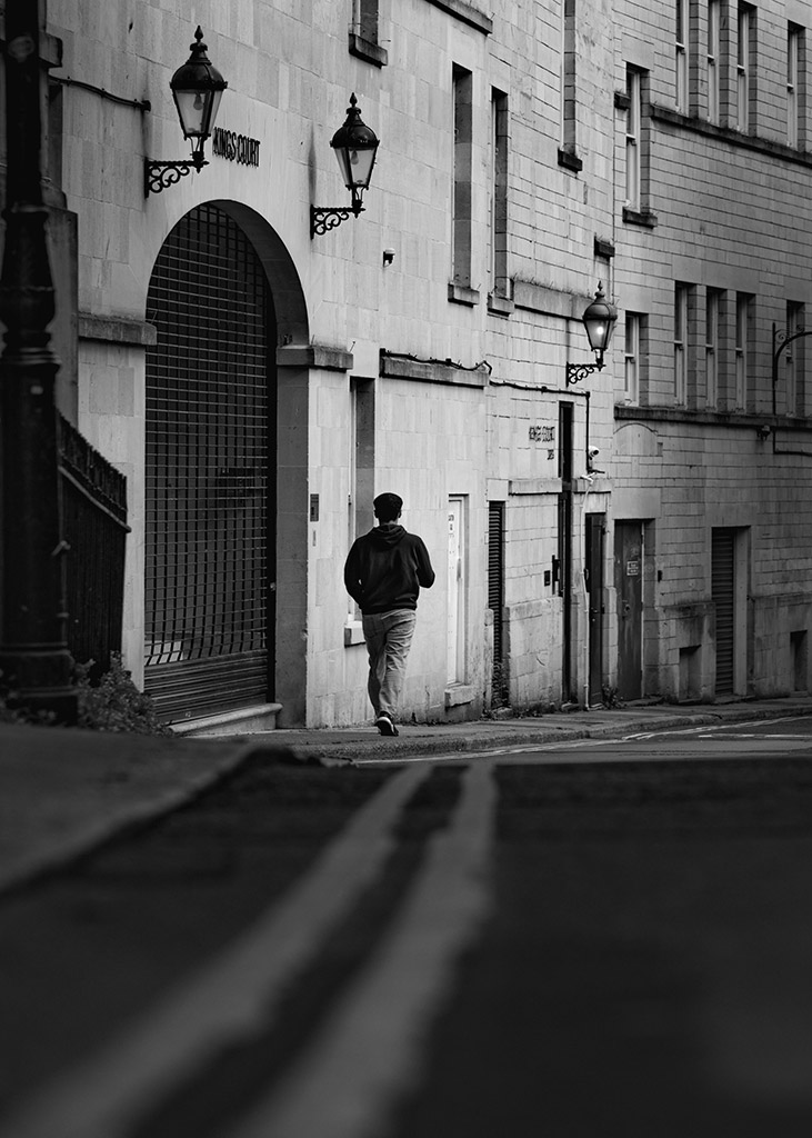 person walking down street through shadows into the light gap