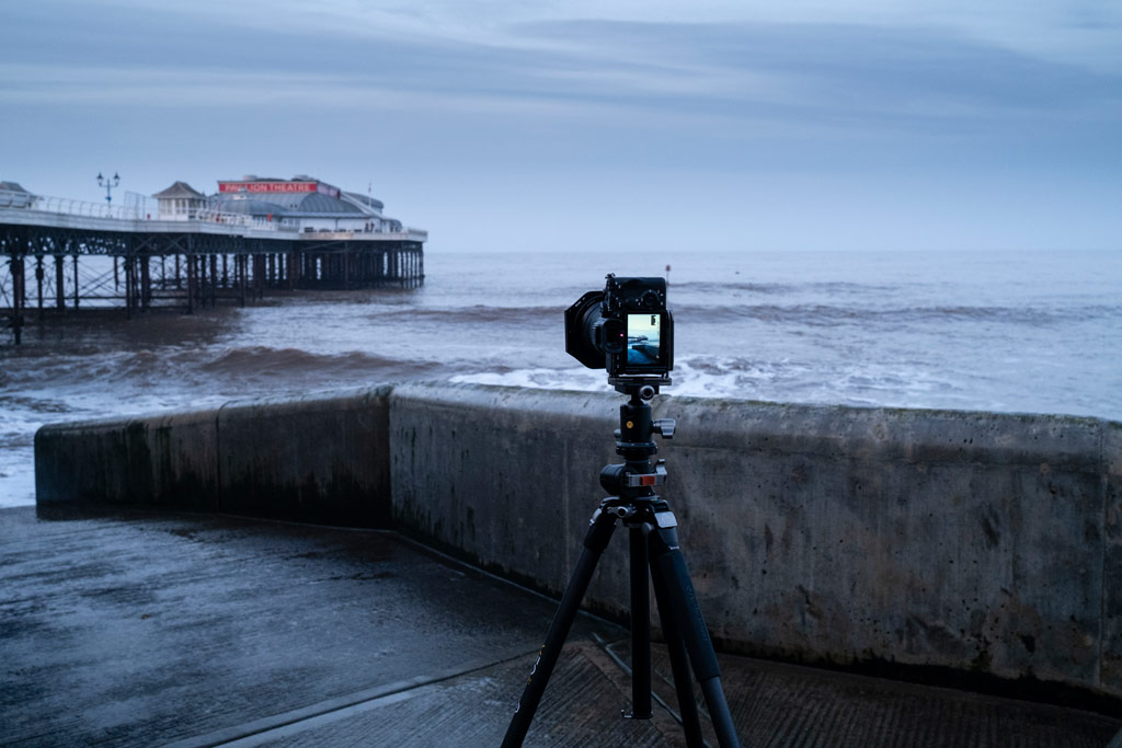 Camera on a tripod shooting a seascape with a pier after sunset