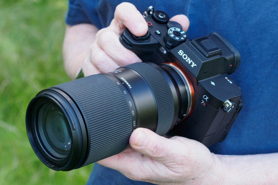 Hands holding Tamron 50-300mm f/4.5-6.3 lens mounted to full-frame Sony Alpha camera