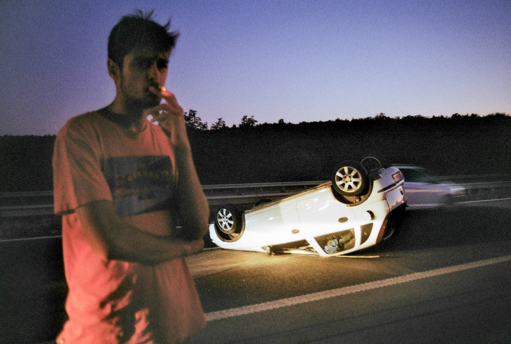 image of car flipped in the background and man in tshirt stood in foreground smoking life as you see it runner up