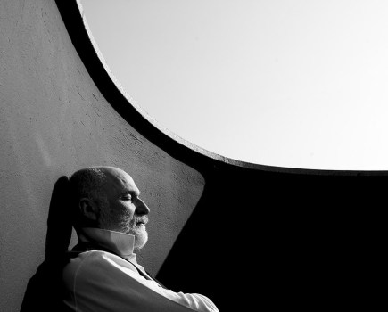 portrait of balding man sat against wall of terrace with eyes closed