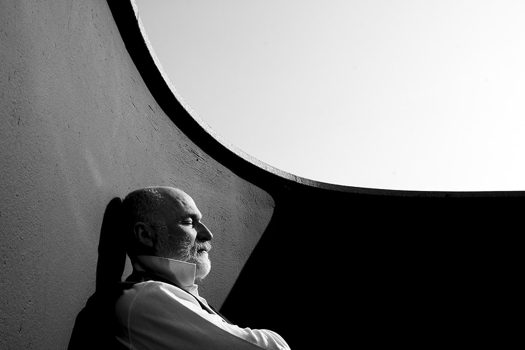 portrait of balding man sat against wall of terrace with eyes closed