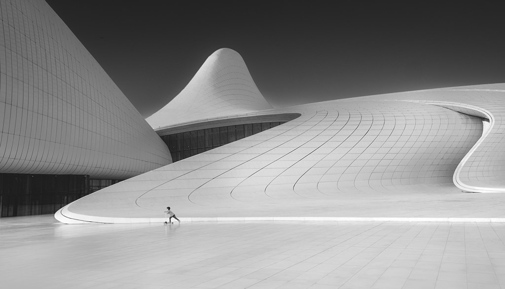 black and white photo awards Architecture Category: Winner: Florian Kriechbaumer - Architectural Playground A child rides a scooter across the plaza of the flowing lines of the Heydar Aliyev Center. The design by the late Zaha Hadid, was meant to break from the rigid forms prevalent in most of Baku's Soviet legacy architecture, and bring a more playful and gentle tone to the city.