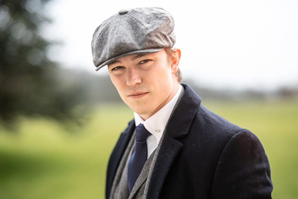 Portrait of a young man in a suit and flat cap shot with flash outdoors