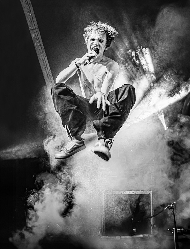 black and white image of singer jumping mid air infront of smoke