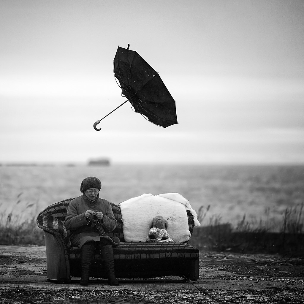 comical photo of woman sat on sofa outside and umbrella flies overhead