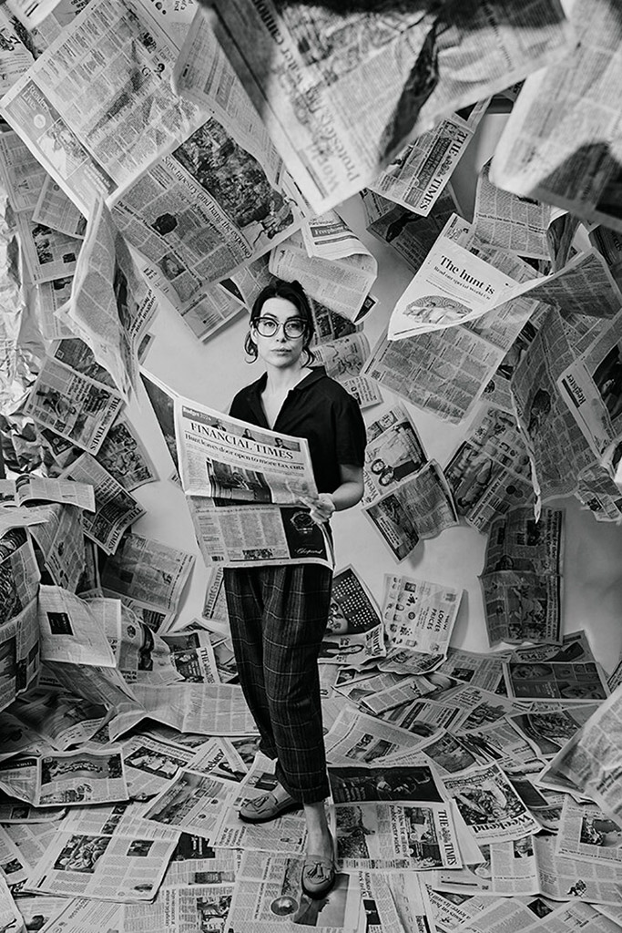 woman stood in room filled with newspapers holding a newspaper