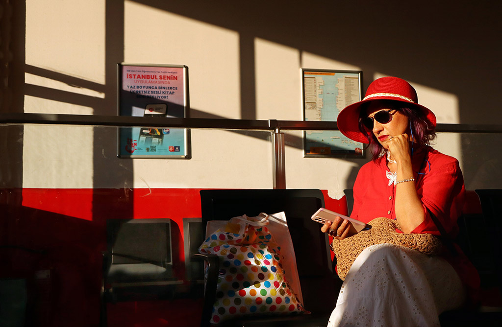 Woman dressed in red with red hat sat in contrasted setting of bright sunlight through the window and long shadows