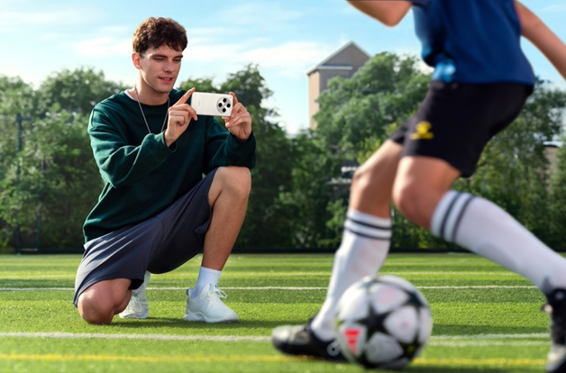 person taking photo on smartphone of boys playing football